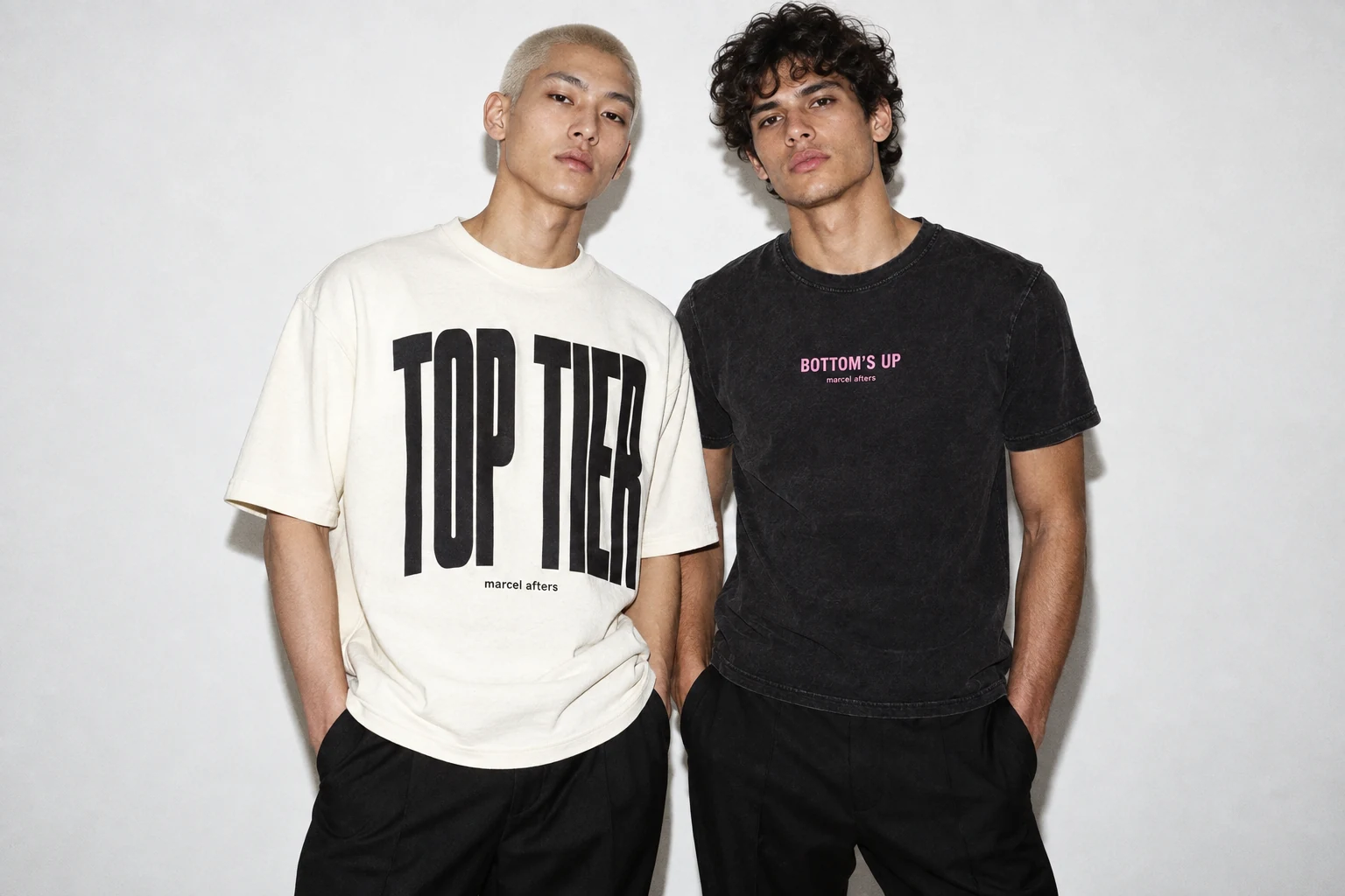 Two adult men wearing Marcel Afters Top Tier and Bottom’s Up statement shirts against a minimal white background